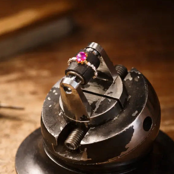 Handcrafted ring secured in a jeweller’s vice on a worn wooden workbench, softly lit to reveal the textures of metal, tools, and the quiet moment of making.