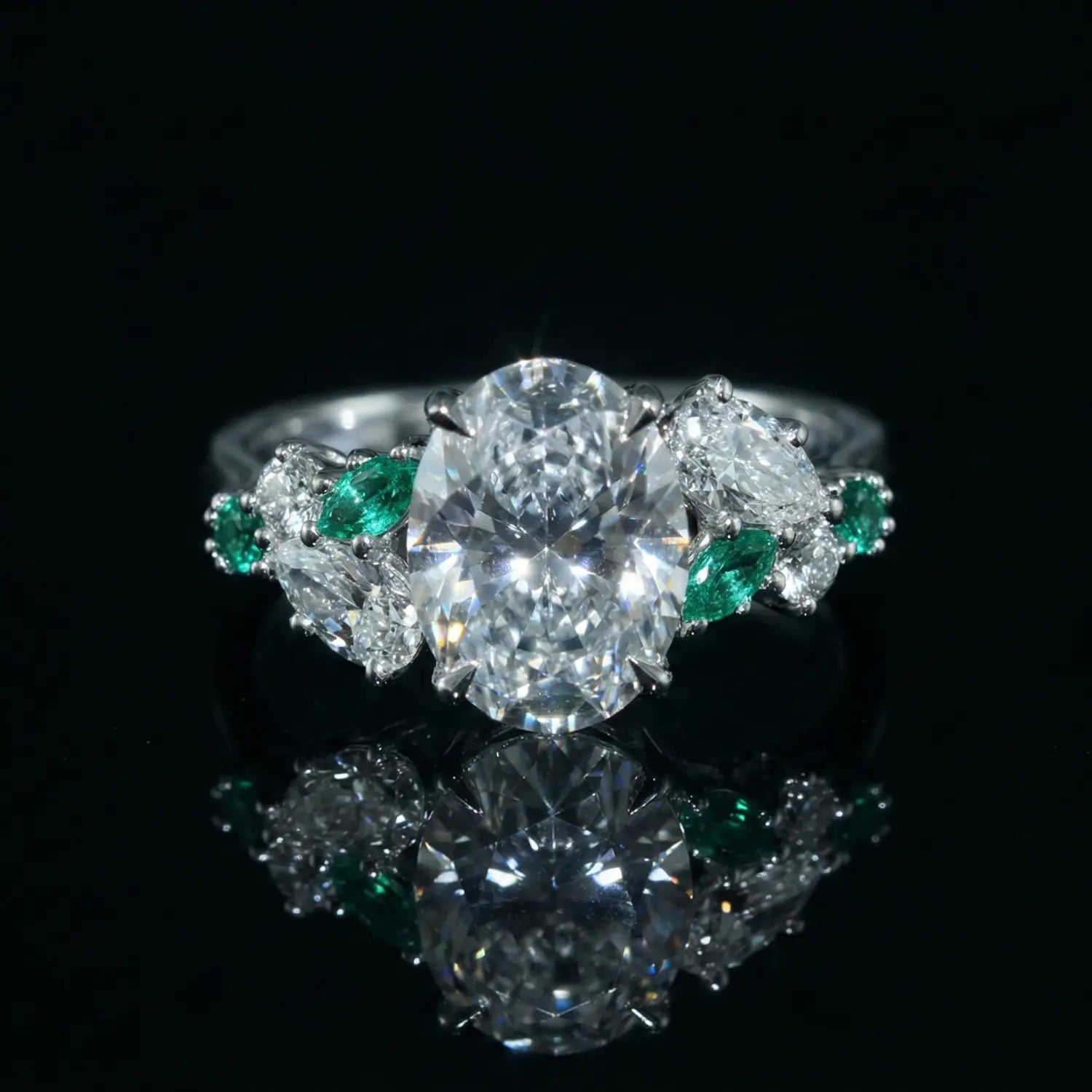 Oval-cut diamond engagement ring in platinum with pear-shaped diamond and emerald side stones, handcrafted by Dimis Designs with heirloom-quality detail.